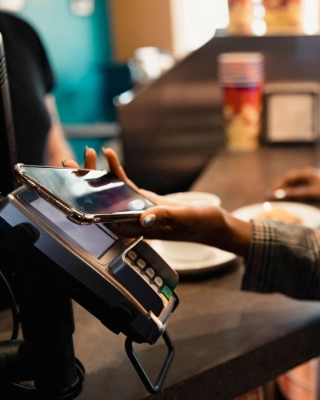 Eine junge Frau bezahlt an der Kasse kontaktlos mit dem Smartphone, ohne Portemonnaie.